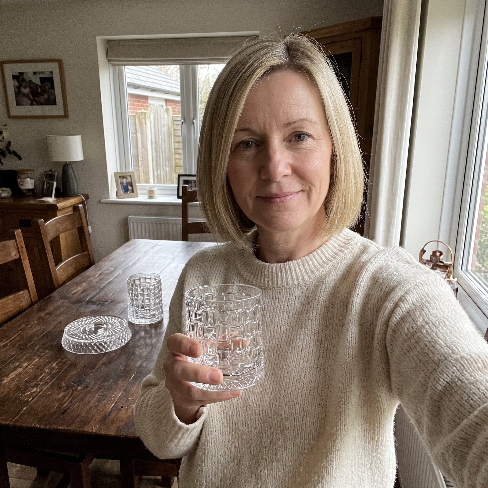 Woman holding a grid glass beside a dining-room window