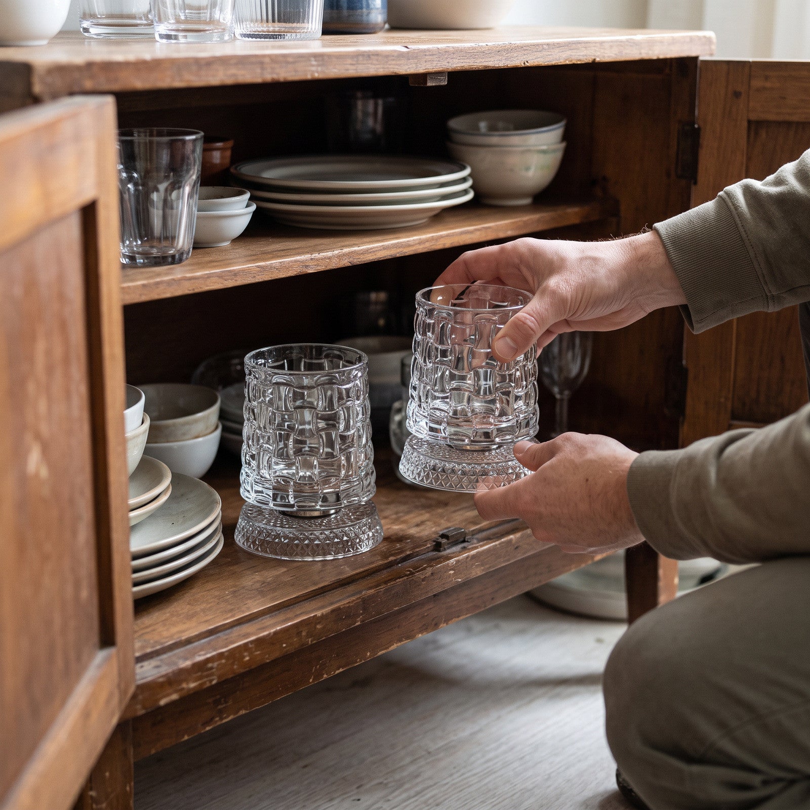 Hand placing a grid glass pair in a low wooden cabinet